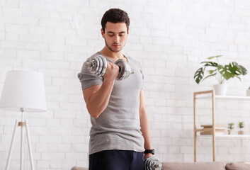 Workout at home. Man with fitness tracker doing exercises with dumbbells in interior