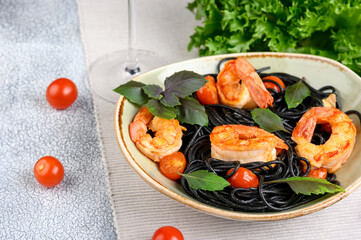 Black plate with black Nero spaghetti with langoustines, cherry and garlic, green lettuce leaves...