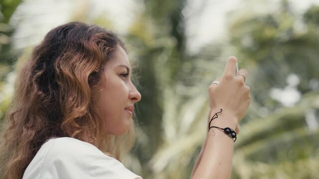 a woman is taking picture on her phone in the jungle while camera is rotating and moving around her. Close-up of full 360 degree rotation. Tracking Arc Shot