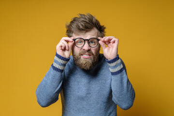 Shaggy, bearded man in an old sweater with a strange expression on face holds glasses in hands and tries to see something.