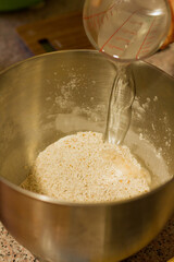 Close up of female hand pouring water into a dish with flour.