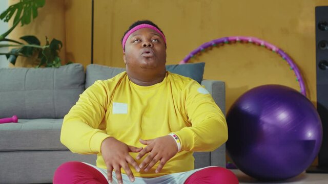 Relaxed afro-american plump man wearing colorful sportswear, practicing yoga moves, meditating and doing asanas during home training.