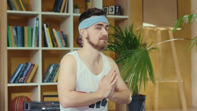 Young caucasian comical man wearing fitness outfit and practicing yoga. Silly jerk retro guy doing meditating asana and spying others opening eyes. Fitness parody concept.