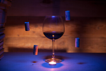 A glass of red wine with flying corks in blue light