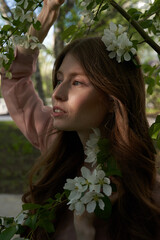 A young girl with blond hair, she stands in the foliage of Apple trees looking away