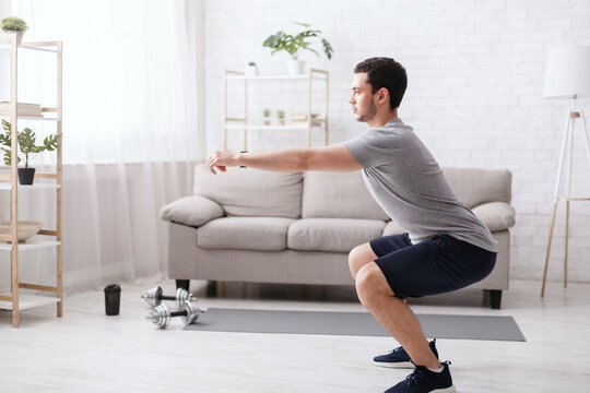 Stay home alone to workout. Man squats in living room interior at home