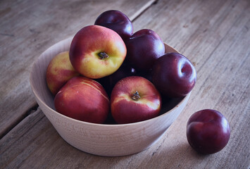 A wooden bowl of plums and nectarines on a rustic kitchen table