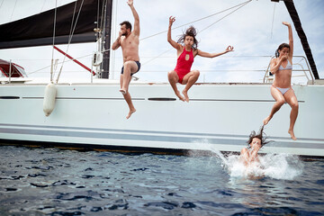 Friends jumping from sailboat on sea ocean trip.