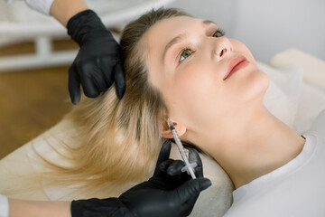 Cropped image of hands of female beautician making injection of vitamins and minerals in the scalp. Young woman with hair loss problem receiving injection in clinic. The concept of hair loss.