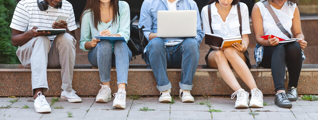 Group of college students studying outdoors with laptop and workbooks, crop