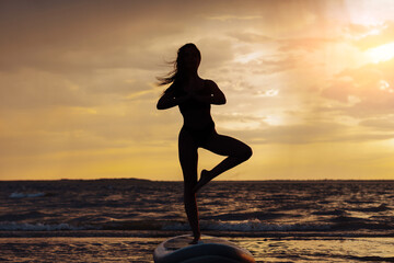 Young sexy woman surfer meditating on her sup board on the sunset. Rest at nature concept