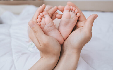 A caring and loving mother holds in her hands the legs and fingers of a small, newborn, sleeping baby on the bed close-up. Woman's happiness. Photography, concept.