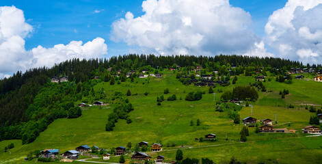 Amazing summer panorama with mountains, small village, green meadows and cloudly blue sky in Swiss Alps. Switzerland.