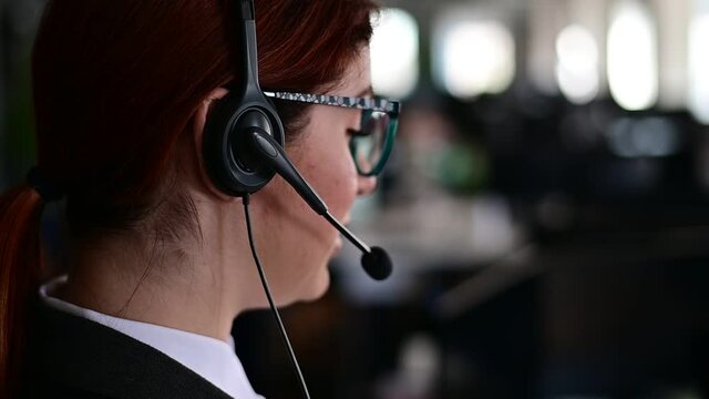 Rear view of a female helpdesk operator. An office manager with a headset answers customer calls. Unrecognizable woman in glasses works as a secretary. Employee call center.