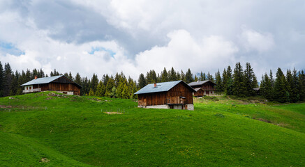 Beautiful view of scenic mountain landscape in the Alps with traditional old mountain chalet and fresh green meadows with blue sky and clouds in spring.
