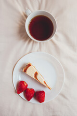 Nice breakfast. Cheesecake, strawberries and a mug of tea on a beige sheet. Beautiful dessert. Food concept flat lay.