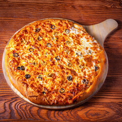 Delicious round pizza on a wooden stand on the table