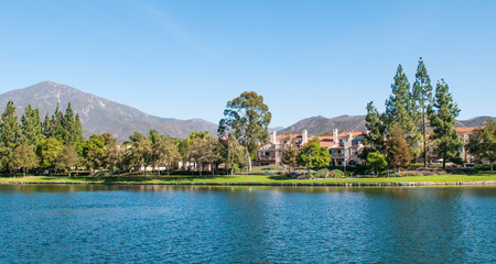 Fototapeta premium Trees nearby a lake with mountains in the background, on a sunny day with blue sky in Rancho Santa Margarita City, Orange County California. USA 