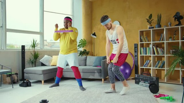 Fake fitness. Multi-ethnic guys go in for sports stretching with resistance band loops doing the wrong way having fun at home training. Retro styled apartment.