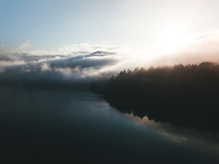Fototapeta premium Moody scenic view of lake against sky. Amazing sunrise above lake and forest with low fog and clouds surrounding the mountains. Serene moment and fantastic scenery at lake Bled, Slovenia
