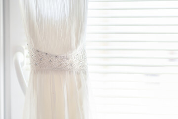 white dress for the bride with rhinestones and lace on the background of a bright window with jalousie