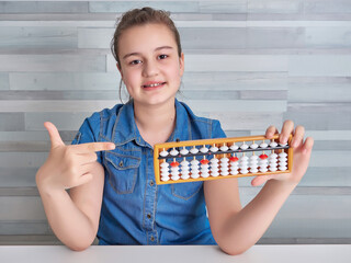 Happy girl in blue blouse holding abacus over light background. Mental arithmetic school. Kids...
