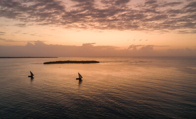 Dhow boats sailing in front of islands during sunrise