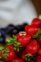 The wedding ring lies on a red ripe strawberry. Summer delicious berries