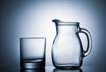 Empty water glass with water jug against blue illuminated background