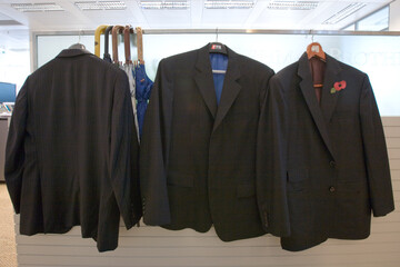 Mens suit jackets hanging in office next to umbrellas