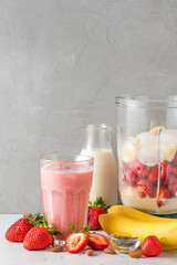 Glass of strawberry and banana vegan smoothie or milkshake made of almond milk with ingredients in...