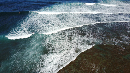 Aerial view on crashing waves, dark green waters with different bottom's colours. 