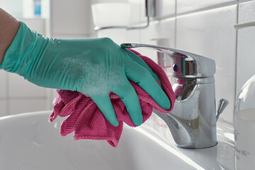 Hand with latex gloves and cleaning cloth cleans bathroom sink faucet