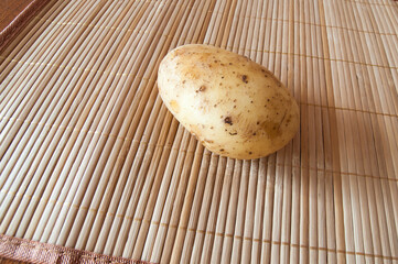 One raw potato lies on a bamboo napkin