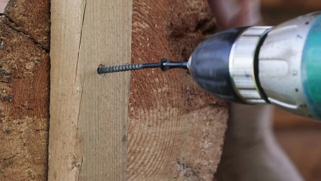 Close-up of an electric screwdriver tightens a screw. We fix the wooden block to the wall of the log house. High quality footage 4K.