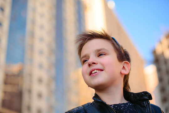Smiling handsome boy looking forward with high-rise building in the background. Positive psychological attitude. Happy and positive thinking. Street photography, close up portrait