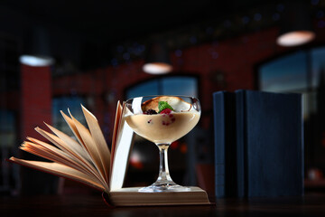 Dessert of berries and ice cream in a tall glass stands on the pages of an open book. The concept of reading and leisure. Copy of the space. Photo in the interior on a dark background.
