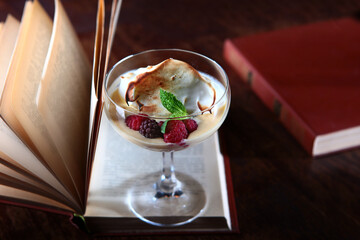 Dessert with berries and cream is on the pages of an open book. The concept of reading and leisure. Copy of the space. Photo in the interior on a dark background. Top view