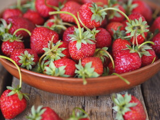 Fresh red strawberries in a clay plate on a wooden background.