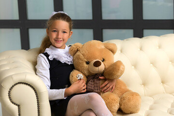 Little girl on sofa hugging teddy bear.