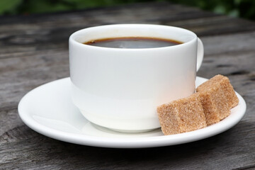 A cup of coffee and cane sugar on a wooden background. White coffee cup and saucer. Espresso coffee. Old wooden table. Morning tasty drrink.