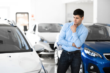 Man Looking At Car Standing In Dealership Showroom