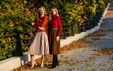 Fashionable clothes. Femininity and tenderness. Friends girls. Fall fashion. Pleated skirt fashion trend. Women walking in autumn park. Autumn stylish outfit. Adorable ladies enjoy sunny autumn day