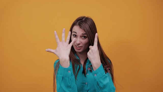 Showing six 6 fingers hand gesture, show the number three with hands, pointing up arm while smiling confident, happy. Young attractive woman with brown hair and eyes, blue shirt, yellow