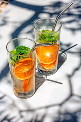 Cold refreshing summer drink lemonade in glasses with metal straws. Detox water or orange cocktail with slices of orange and mint in glass with metal recyclable straw. Summertime zero wast concept