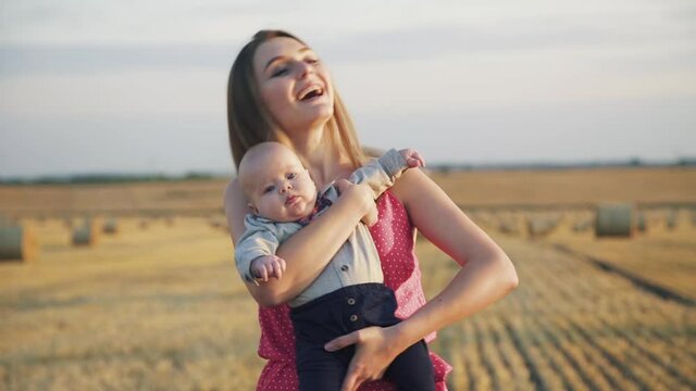 Happy portrait of smiling mother with her baby son in hands having joy in field