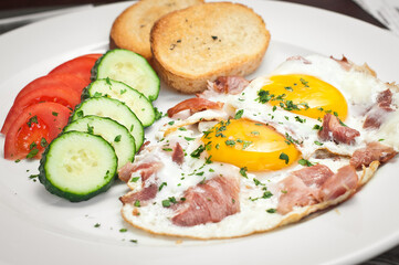 Fried eggs with bacon and fresh vegetables.