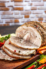 Traditional sliced baked pork garnished with herbs, lemon carrots and spices, prepared for serving on the festive table, close-up, shallow depth of field, selective focus. The concept of delicious