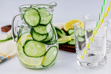 Cold drink made of cucumber and lemons, homemade lemonade in a decanter and two empty glasses, on a white background, shallow depth of field, selective focus. Healthy drinks concept