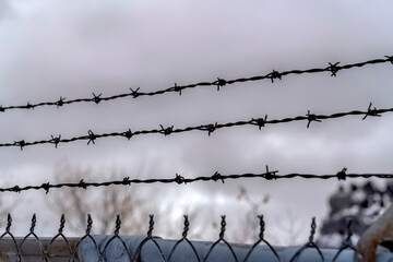 Sharp barbed wires of rusty chain link fence with blurred cloudy sky background